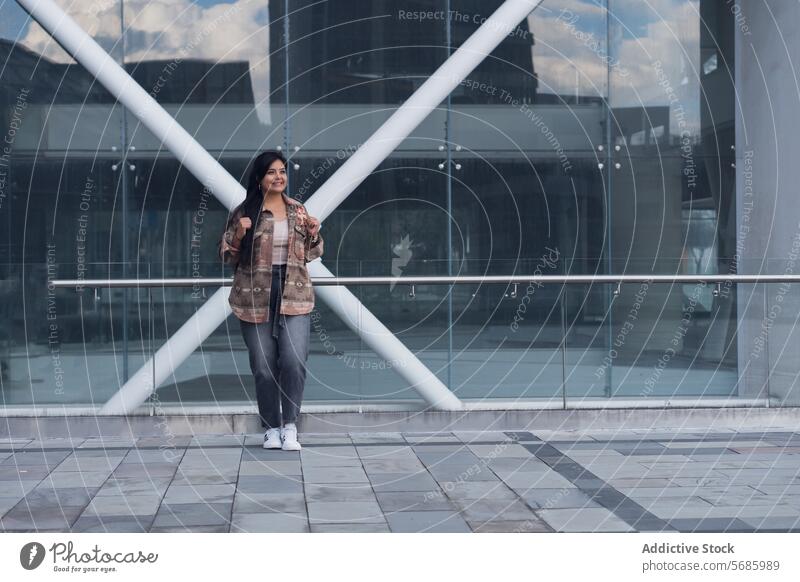 Cheerful woman standing in front of modern building smile positive cheerful street glass casual happy joy female city urban young glad optimist town confident