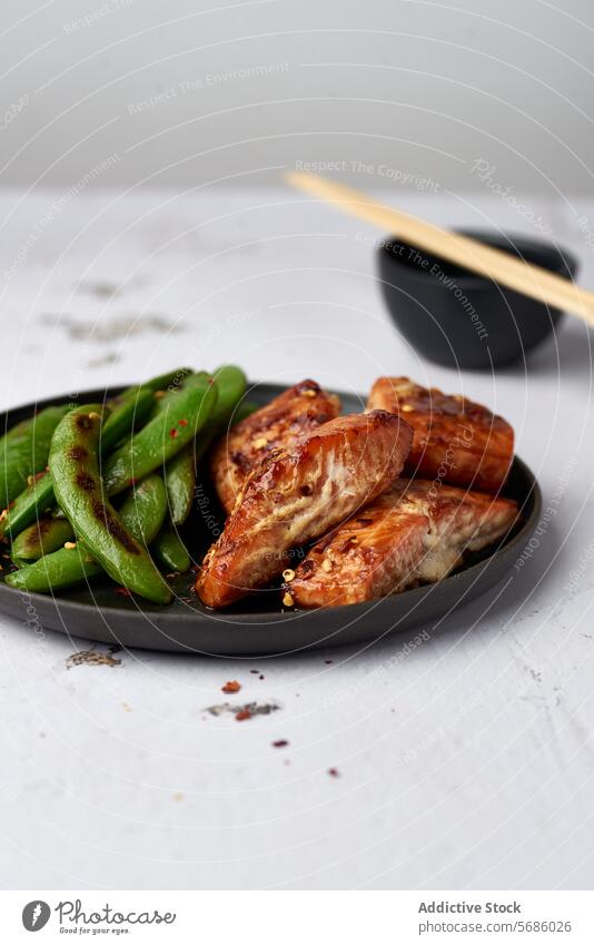 Grilled chicken and snap peas on a modern plate grilled wing black plate chopstick bowl food cuisine meal dinner lunch meat poultry vegetable green asian