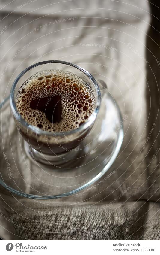 Close-up of fresh coffee in a clear glass cup beverage drink close-up frothy brewed texture fabric backdrop transparent detail caffeine morning refreshment