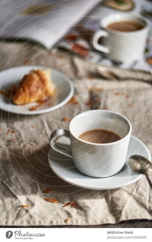 Cozy coffee and croissant breakfast scene table cup linen rustic cozy morning plate spoon fabric texture warm light beverage milk white porcelain silverware