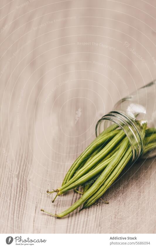Fresh green beans spilling from a glass jar wooden surface fresh vegetable raw tipped cascading healthy food ingredient organic natural pod legume vegetarian