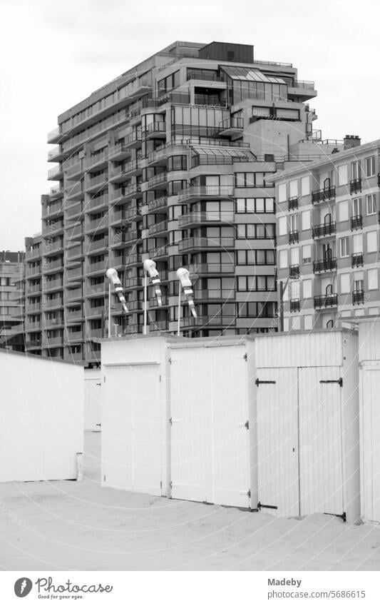 White beach cabins in front of modern high-rise buildings on the beach at Knokke-Heist on the North Sea near Bruges in West Flanders in Belgium, photographed in neo-realist black and white