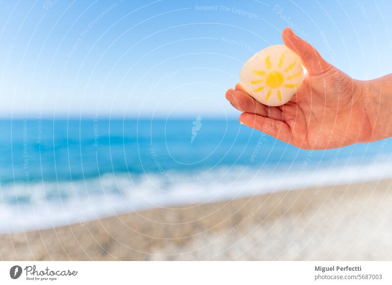 Child's hand holding a beach stone with a sun drawn on it, a defocused beach in the background. sand vacation water summer child beauty concept play relaxation