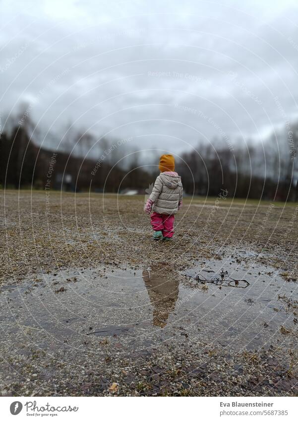 Warmly dressed toddler walks away from a puddle Winter Puddle puddle mirroring Toddler Child Rain Weather Wet Gloomy