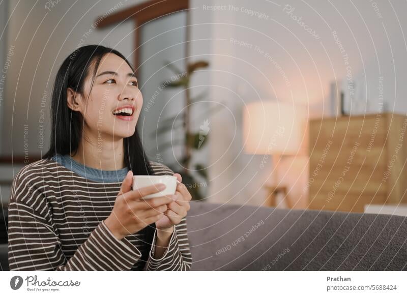 Smiling young woman relaxing with coffee on sofa looking away and contemplating something coffee cup beverage morning living room breakfast home lifestyles tea