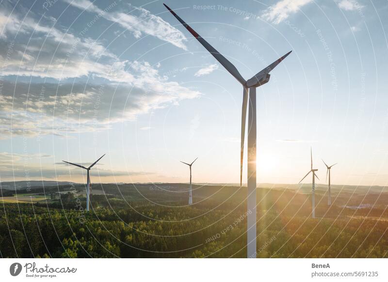 Wind turbines in a hilly forest in front of a partly cloudy, but sunny sky are seen from an aerial view during sunset Aerial Clean Cleantech Country Countryside