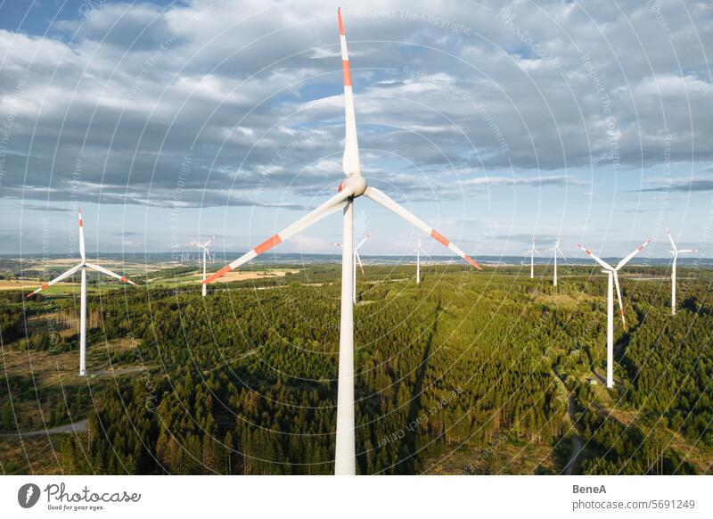 Wind turbines in a hilly forest in front of a partly cloudy, but sunny sky are seen from an aerial view during sunset Aerial Clean Cleantech Country Countryside