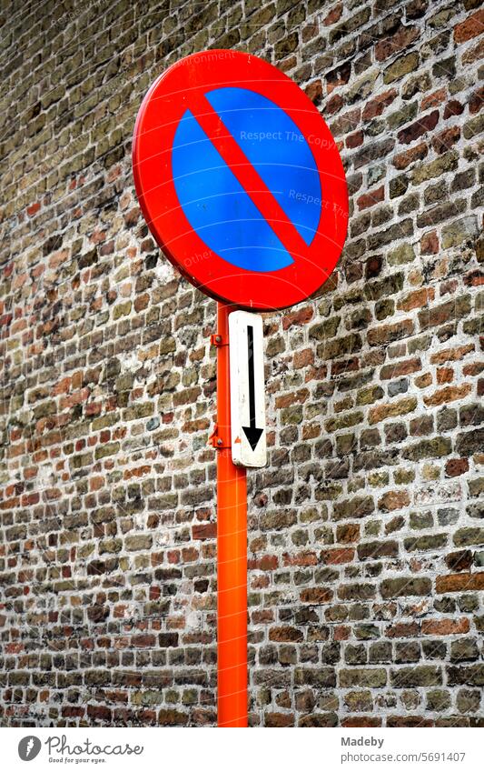 No stopping traffic sign with arrow in red and orange in front of an old brick wall and facade in the alleys of the old town of Bruges in West Flanders in Belgium