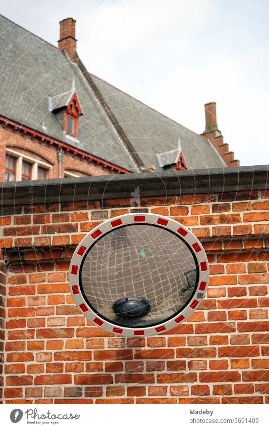 Round traffic mirror with reflection of the pavement in front of a brick wall in red-brown of an old school in the alleys of the old town of Bruges in West Flanders in Belgium