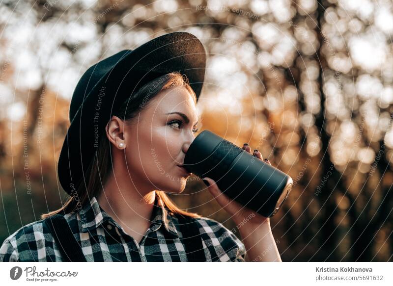 Hipster woman drinking hot coffee or tea, thermos, golden park, forest in autumn attractive background beautiful beverage break carefree caucasian coffee cup