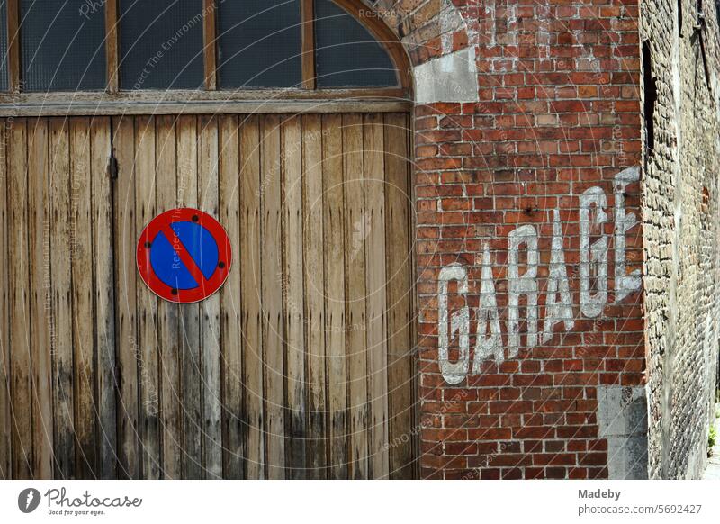 Old faded white lettering Garage in capital letters on the old reddish-brown brick wall of a garage with a no-stopping sign in the alleys of the old town of Bruges in West Flanders in Belgium