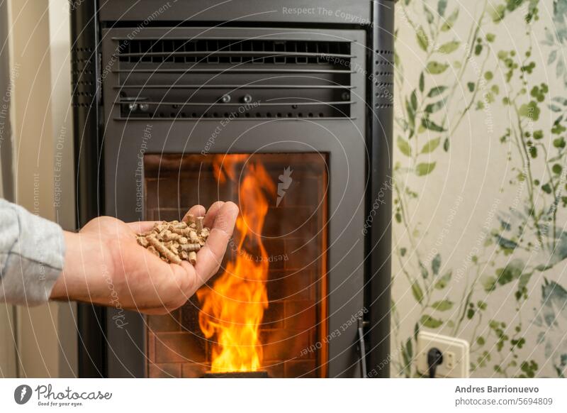 Man's hand holding pellets in front of the glass of a stove with a beautiful flame, sustainable and ecological heating ecology fuel recycling economy