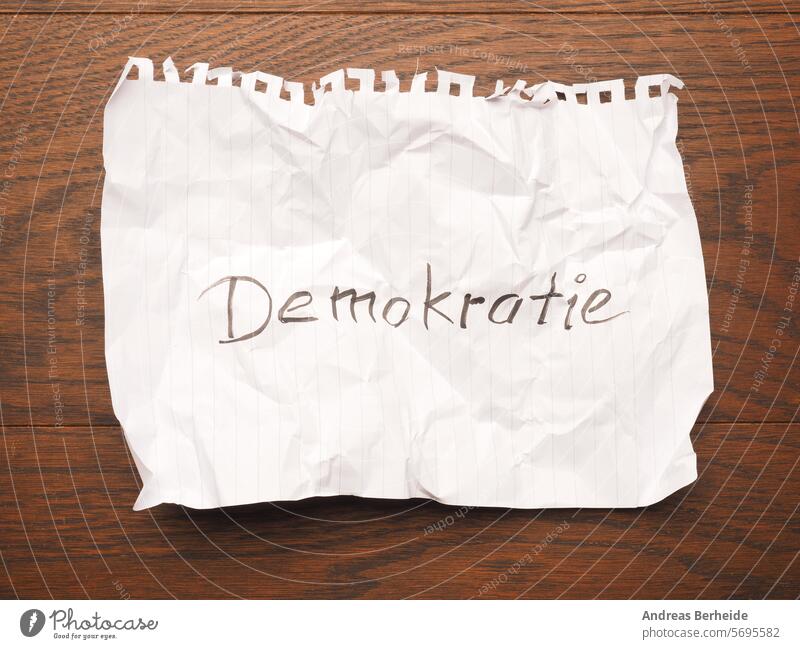 Crumpled sheet of paper with the word democracy on a wooden table Democracy Peace Global unit Feeling of togetherness Vote Concepts message Idea Decision Study