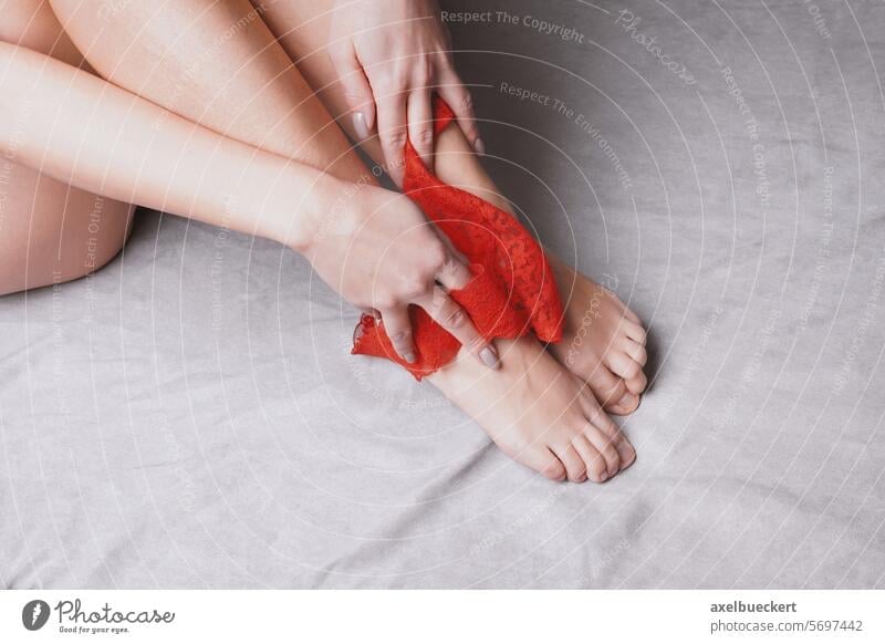 legs of woman undressing in bed pulling down red lace panties to her feet -  a Royalty Free Stock Photo from Photocase
