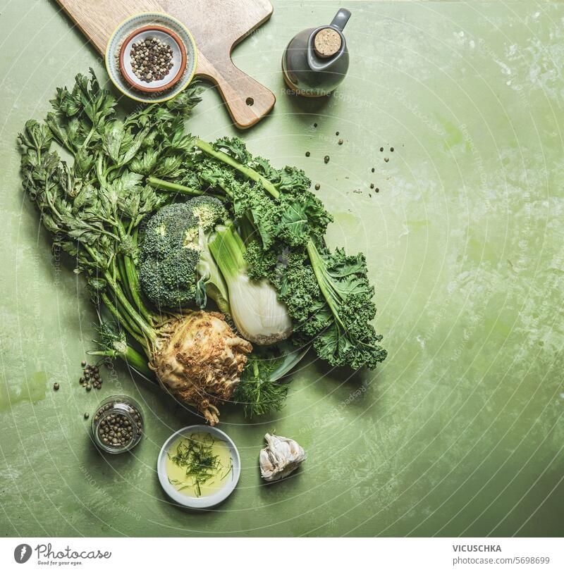 Green vegetables on table background with cutting board and ingredients, top view green celery fennel broccoli kale above overhead flat lay raw variety organic