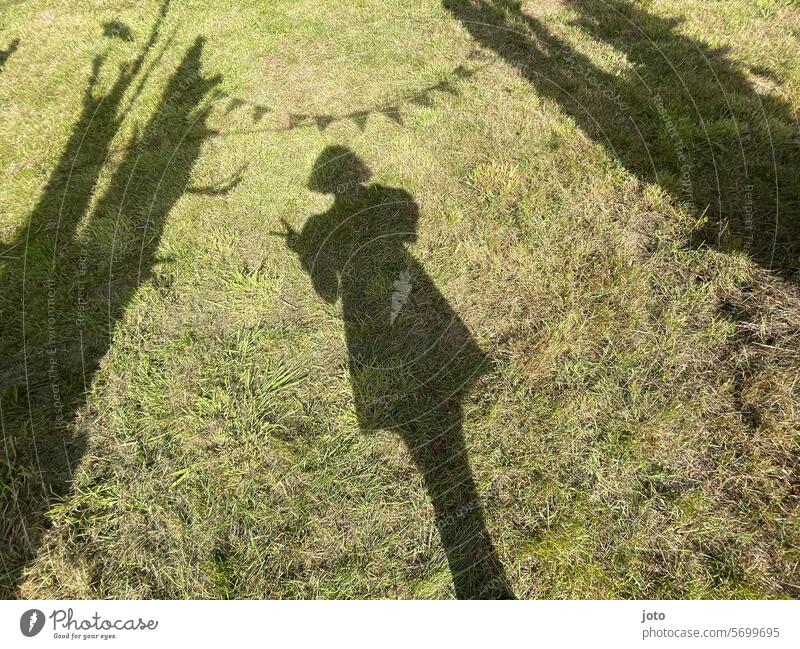 Shadow of a woman in the grass with a pennant chain at a garden party peace sign Peace sign Shadow play Silhouette Party goer Party mood Party dress Summertime