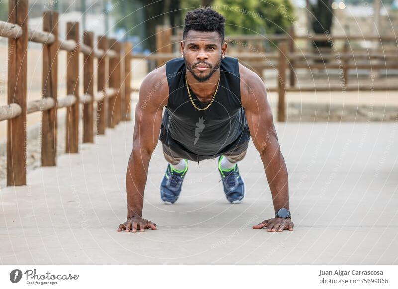 Strong sportsman doing plank in city park athlete warm up push up abs power core exercise muscle male young african american black ethnic afro sportswear ground