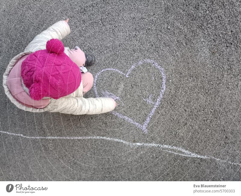 Child with pink cap paints heart on street with street chalk Love Heart Painting (action, artwork) Street painting Chalk Children's drawing Asphalt