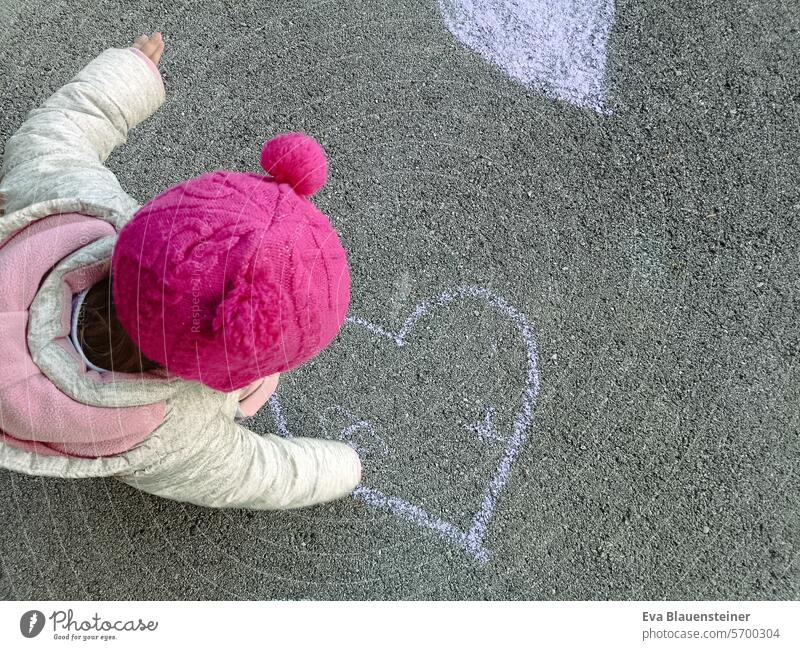 Child with pink cap paints heart on street with street chalk Love Heart Painting (action, artwork) Street painting Chalk Children's drawing Asphalt