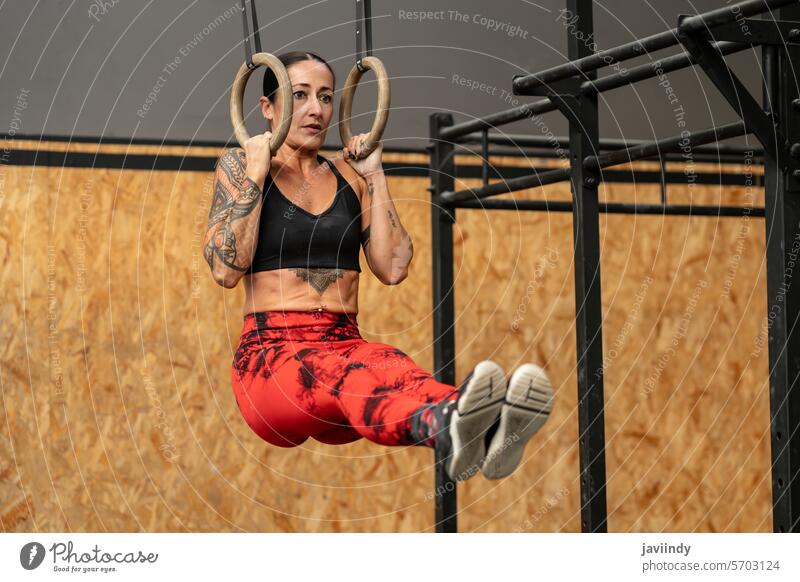 Woman performing core exercises hanging from olympic rings woman cross training gym fitness strength workout athletic suspension abdominals muscles challenge