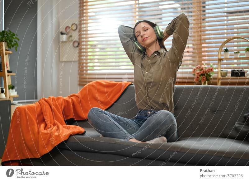 Happy young woman listening favorite music in headphone relaxing on couch at home relaxation recreation technology sofa entertainment living room smiling