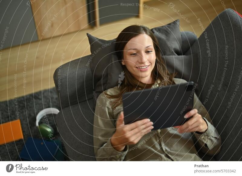 Smiling young woman lying on couch and surfing internet or watching video on digital tablet technology winter using home online shopping communication
