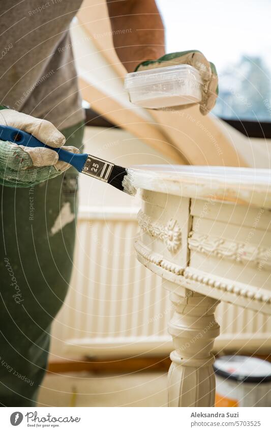 Middle-age man painting old wooden table with paint brush in white color. Furniture restoration, DIY repair, repair by oneself and home improvement. Recycling and sustainable lifestyle
