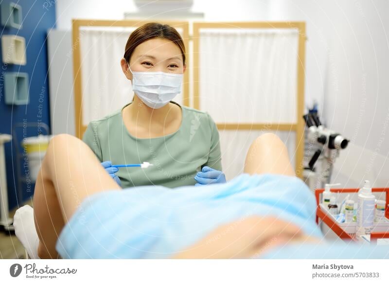 Gynecologist examines a patient laying on gynecological chair using medical vaginal speculum. Doctor takes a smear from a young woman cervix. Diagnosis of diseases.