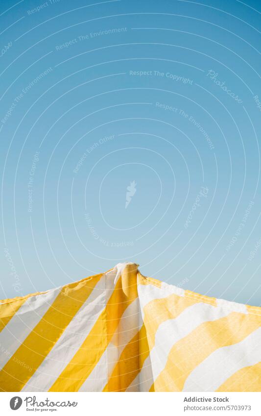 Striped yellow and white sunshade against clear sky stripe blue minimalistic summer relaxation contrast vibrant color leisure vacation sunny outdoor simplicity