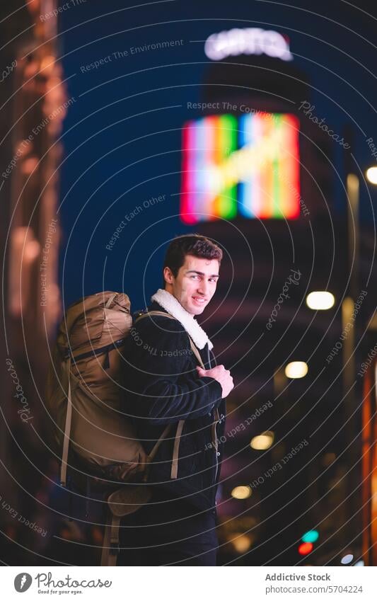 Smiling young man with a backpack on a neon-lit street in Madrid, turning to look at the camera smiling urban night city male adult travel happy vibrant fleece