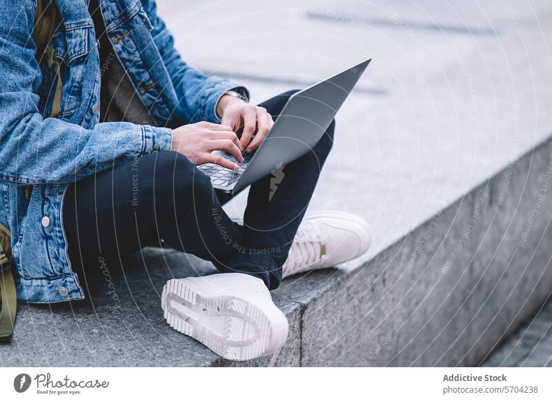 Young man works on his laptop while seated on the steps in a lively Madrid square young working outdoor city life denim jacket urban adult computin freelance