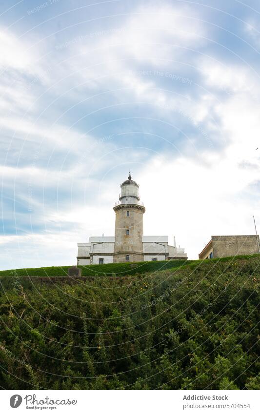 Lighthouse on green grassy hill in countryside under cloudy sky lighthouse beacon picturesque guide environment hillside architecture building landmark