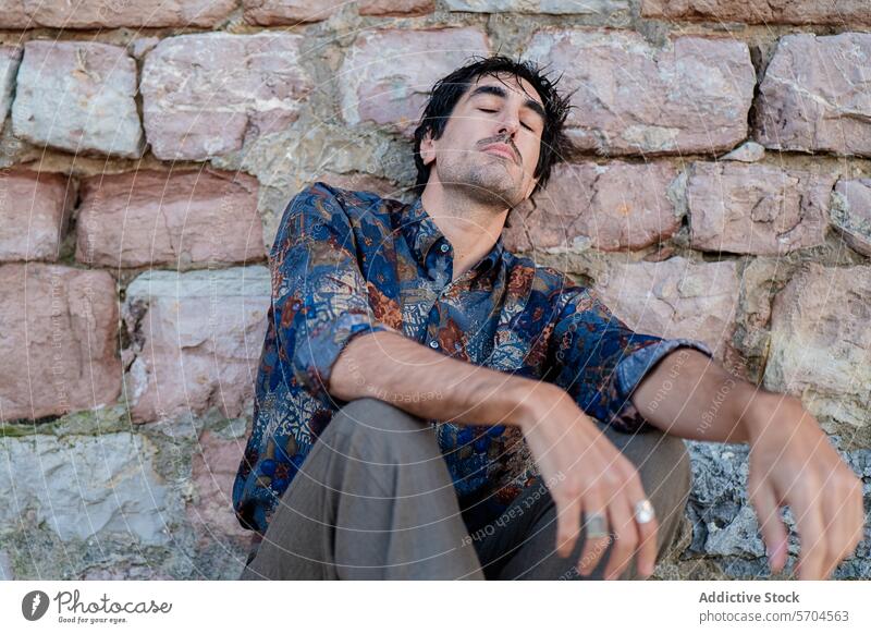 Contemplative man sitting by a rustic stone wall contemplative thought young expression pensive aged lost in thought casual individual outdoors daytime