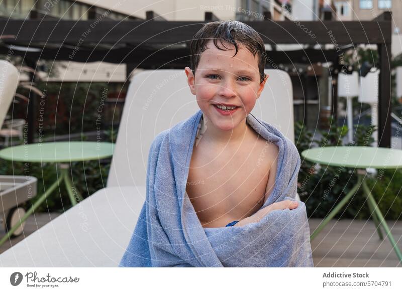 Young boy wrapped in towel smiling outdoors child happy wet hair sitting leisure blue young cheerful joy summer relax relaxation casual lifestyle comfort