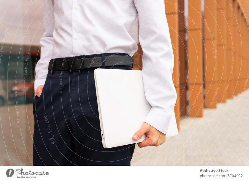 Close-up of a professional anonymous man in a white shirt and navy pants holding a laptop, ready for a productive business day Man technology modern