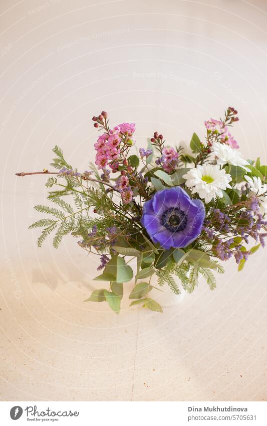 beautiful flower bouquet with purple anemone and pink wax flower on white beige neutral background copy space top and bottom. Floral arrangement vertical backdrop.