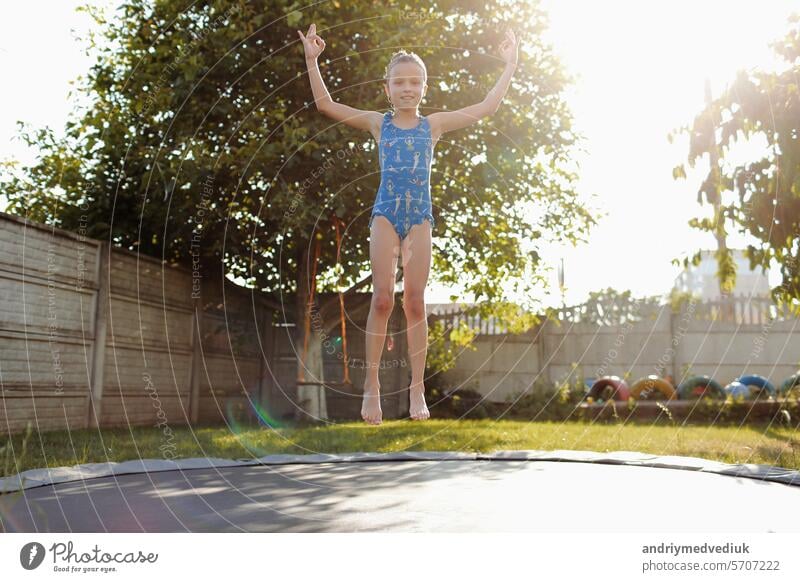 little sports girl jumps on a trampoline. Outdoor shot of girl jumping on trampoline, enjoys jumping in home. happy summer vacation child fitness kid nature sun