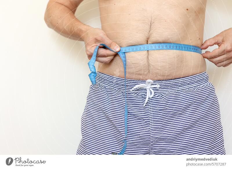 Man measures his fat belly with measuring tape and shows thumb up. Concept of weight loss, health problems of obese people. Controlling eating and active lifestyle. World Obesity Day