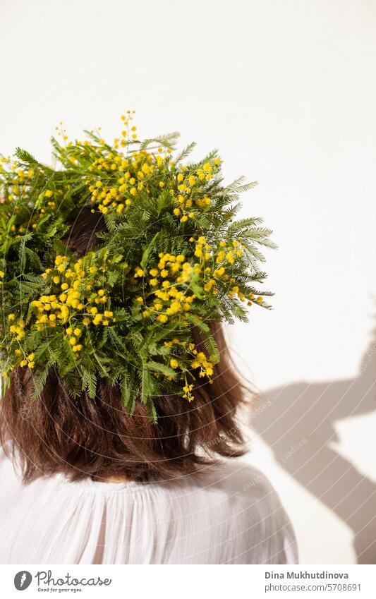 female florist holding beautiful bouquet with yellow mimosa spring flowers, ranunculus and eucalyptus leaves. Fresh elegant home decor. Florist work. wreath