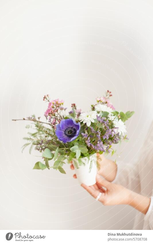 hands holding beautiful minimal bouquet with spring flowers. Purple anemone and eucalyptus leaves. Fresh elegant home decor. Florist work. salon vase florist