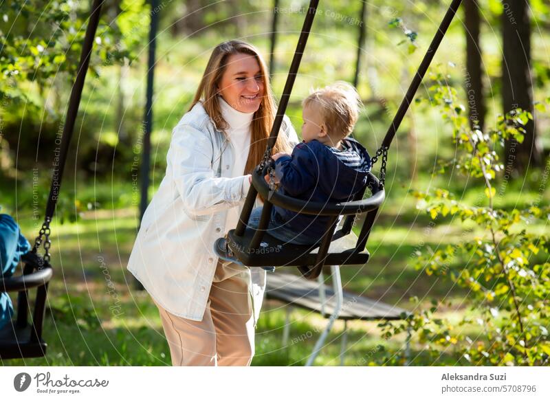 The mother with two children is having a fun time at the playground. The mother is swinging her children on the swings. active activity baby boy care caucasian