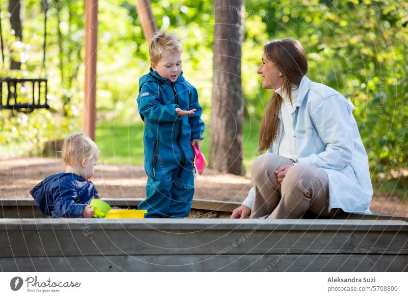 The mother with two children is having a fun time at the playground. Two little boys with their mom playing in the sandbox active activity care casual caucasian