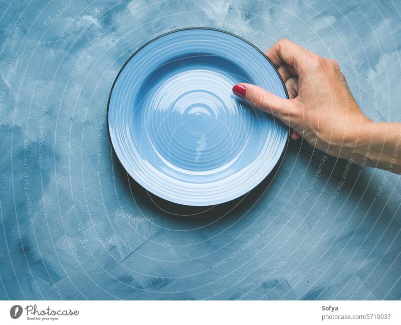 Blue background with plate and woman's hand nail polish red ceramic tableware dinnerware dish eat lunch concept food abstract empty blue texture gray pastel