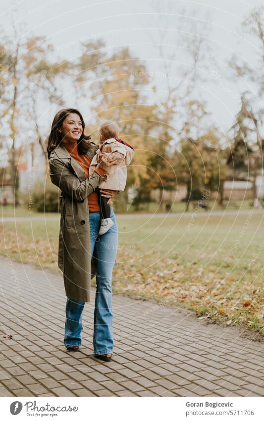 Young woman holding cute baby girl in the autumn park small caucasian mother outside daughter child little love happiness together family play mom smile season