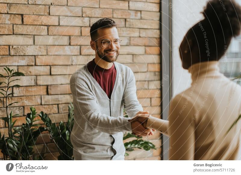Young multiethnic business couple handshaking in the modern office adult african american black businessman businesspeople businesswoman businesswomen caucasian