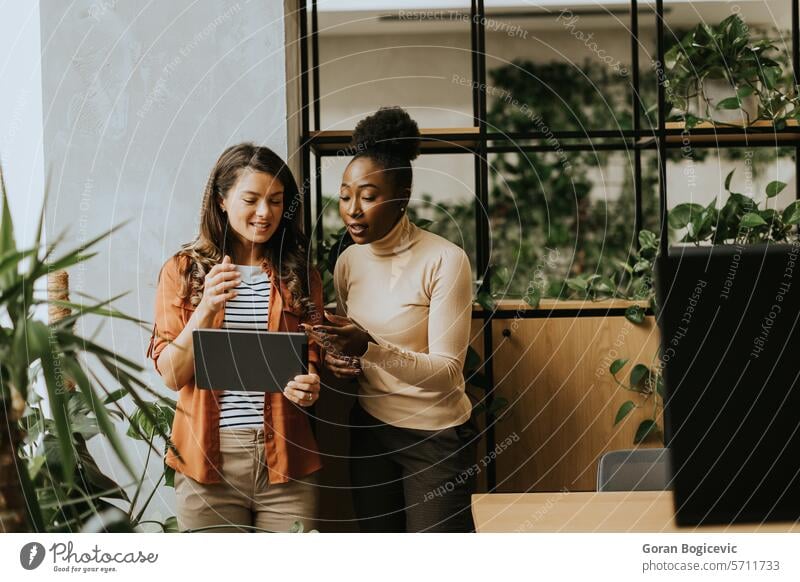 Two young business women with digital tablet standing in the modern office adult african american black businessman businesspeople businesswoman businesswomen