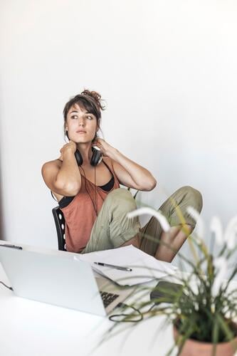 A young woman takes a break from her creative work reflection headphones pen thought project contemplative pause casual inspiration pondering relaxed thinking