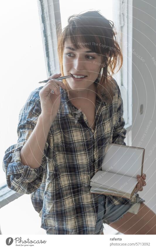 A contemplative young woman holds a pencil and a blank notebook, ready to jot down creative ideas. thoughtful plaid shirt inspiration writing casual artist