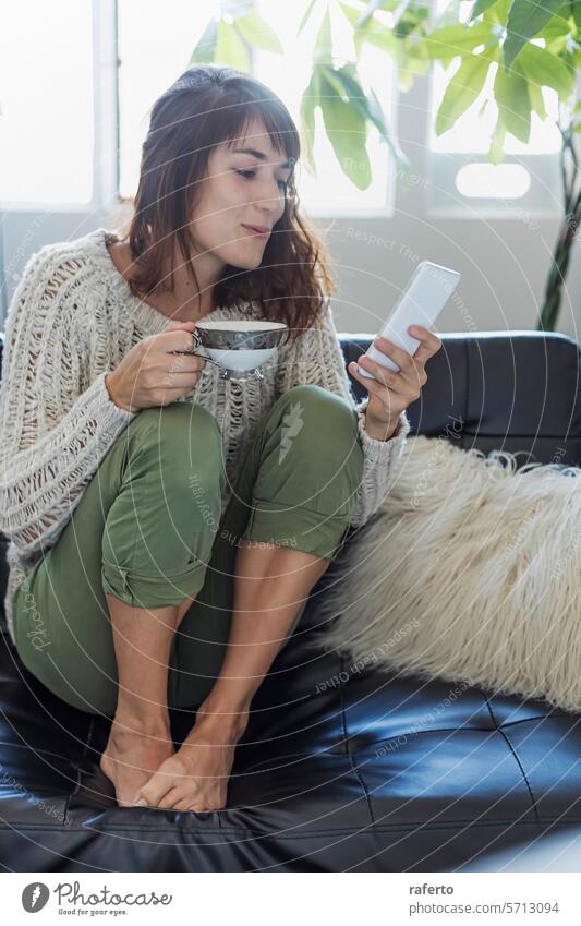 A cozy moment with coffee and a smartphone. woman knit-sweater leisure relaxed modern sunlit peaceful morning contemporary living technology comfort everyday