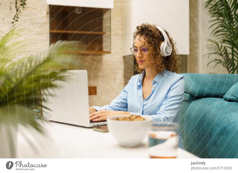 Positive woman in headphones typing on laptop while in living room freelance remote work home positive project female online job internet browsing telework